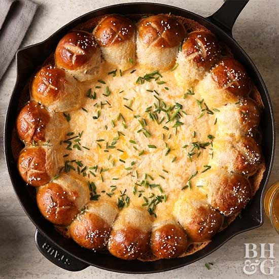 a skillet filled with bread and cheese on top of a table next to a jar of mustard