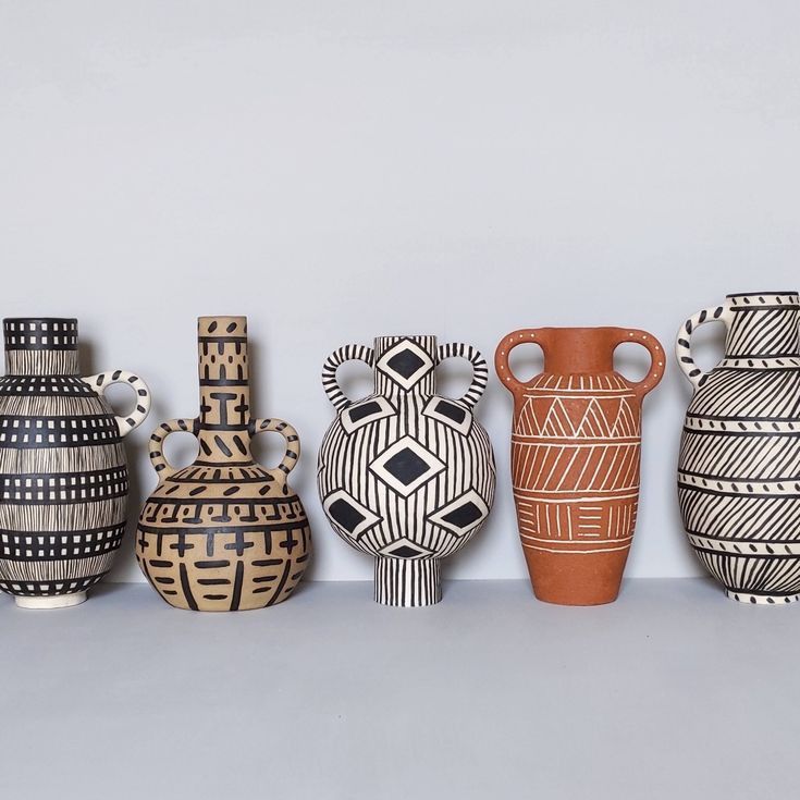 five vases are lined up on a shelf in front of the wall, one is painted black and white