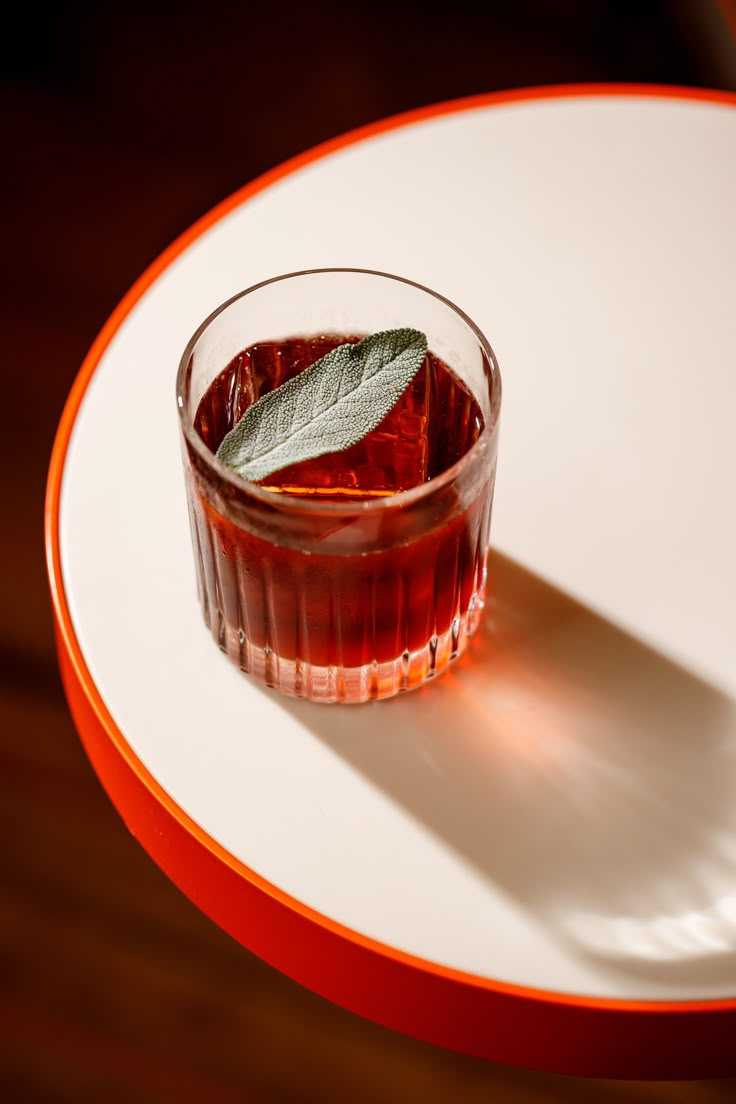 a glass filled with liquid sitting on top of a white plate next to a green leaf