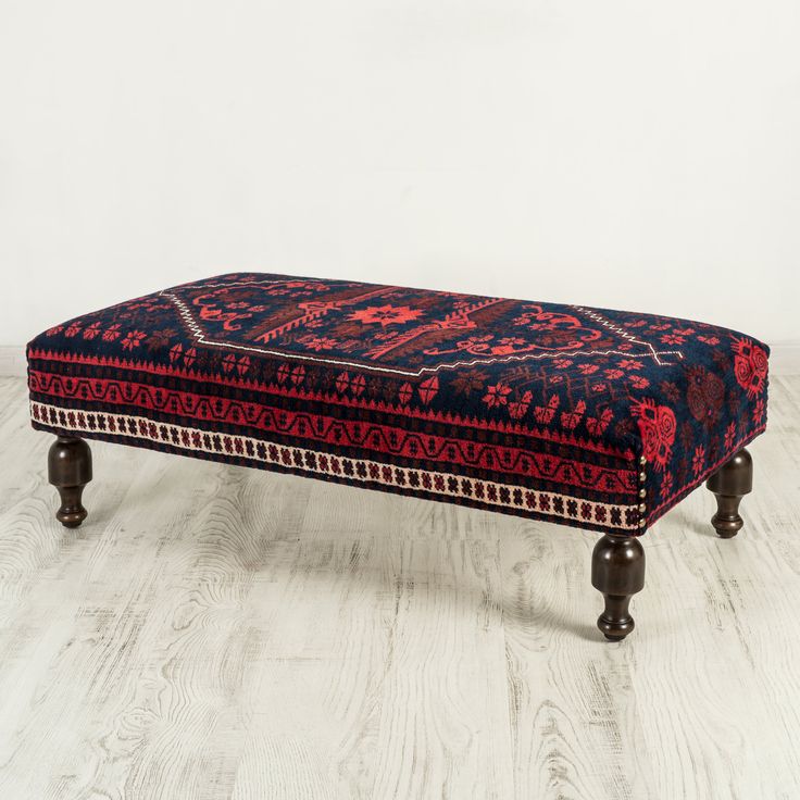 a red and black ottoman sitting on top of a wooden floor next to a white wall