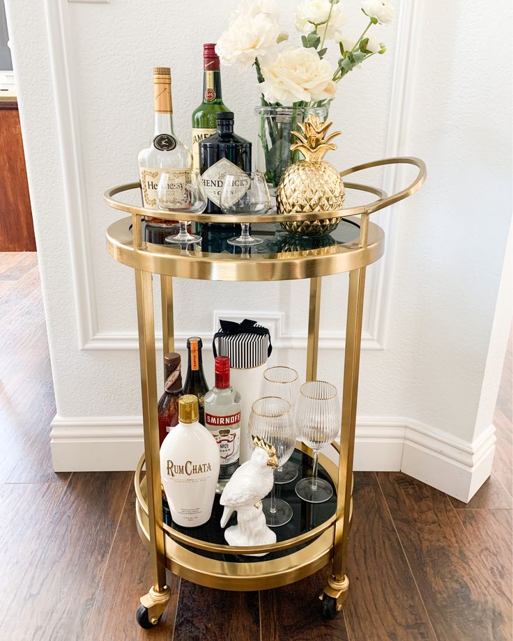 a gold bar cart filled with liquor bottles and glasses on top of a hard wood floor