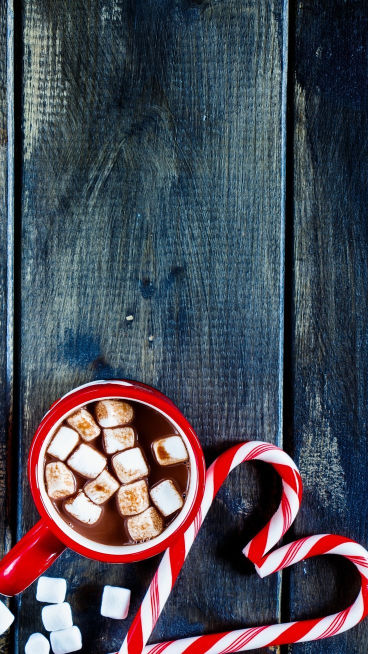 hot chocolate with marshmallows and candy canes on a wooden table top