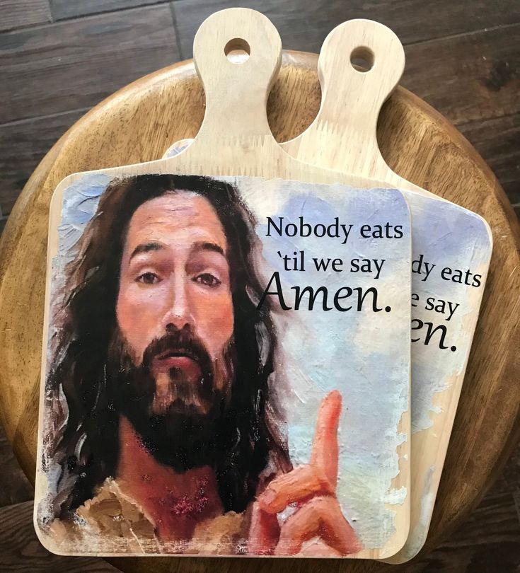 a wooden cutting board with an image of jesus pointing to his right and saying nobody eats till we say amen