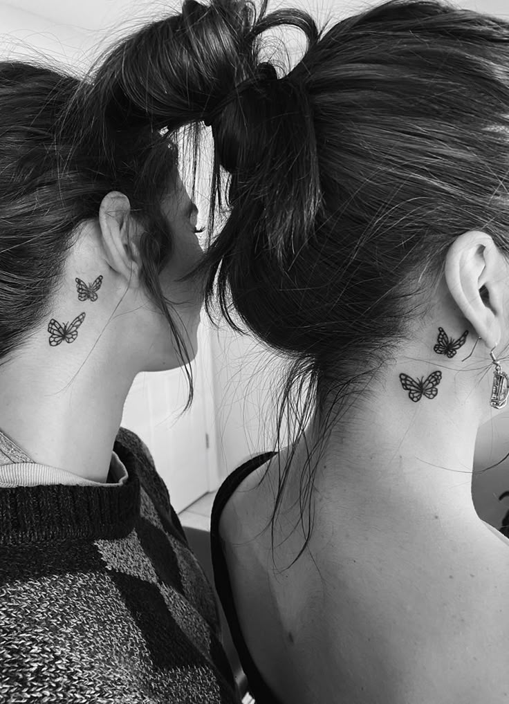 two women with butterfly tattoos on their neck and behind their backs, both looking at each other