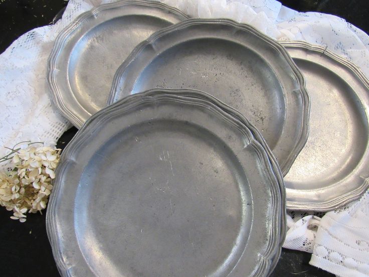 three metal plates sitting next to each other on a white lace doily with flowers in the background