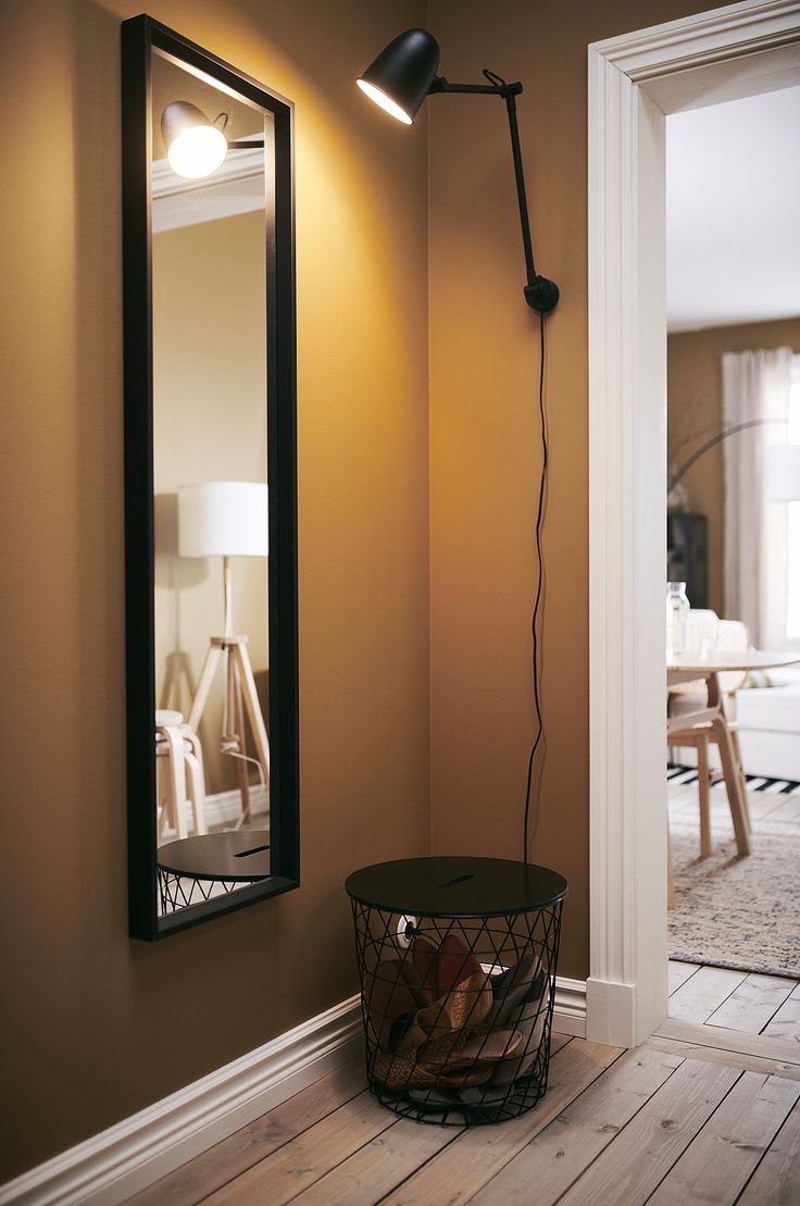 a room with a mirror and lamp on the wall next to a basket in the floor