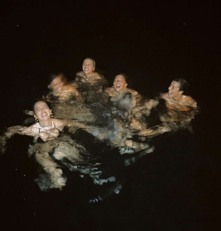 five people are floating in the water at night with their heads turned to look like they're swimming