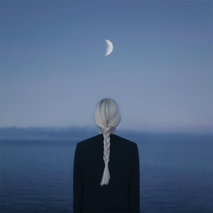 a woman with long white hair standing in front of the ocean looking at the moon