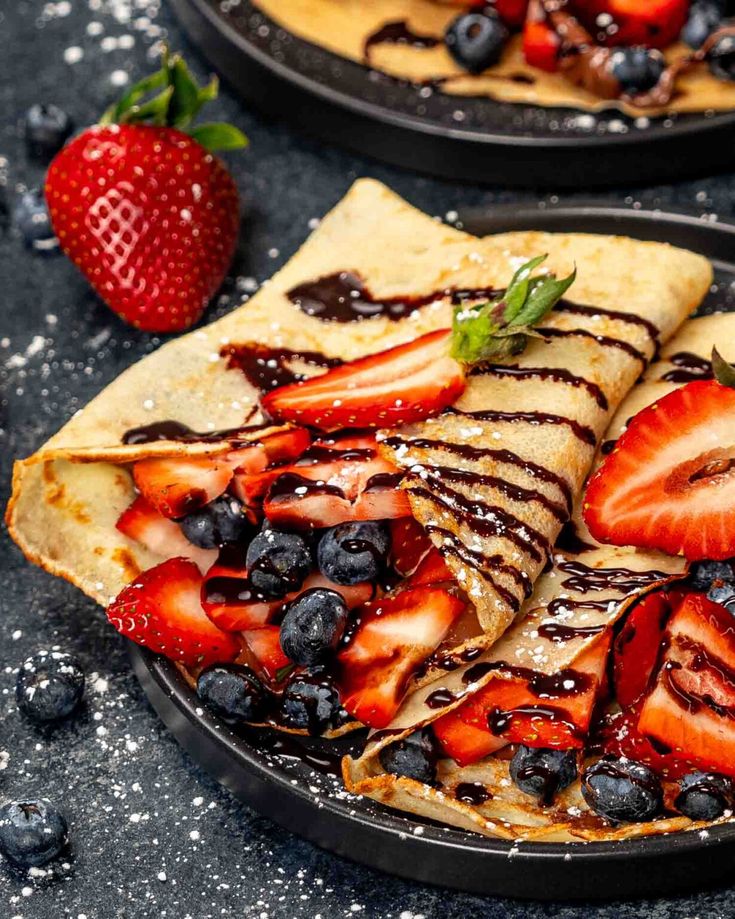 two pancakes with strawberries and chocolate drizzled on them, one is cut in half