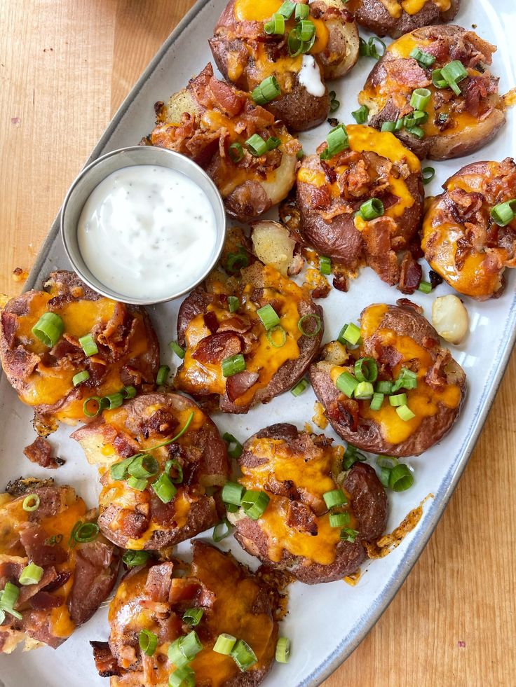 a platter filled with potato skins covered in cheese and green onions next to a small bowl of ranch dressing