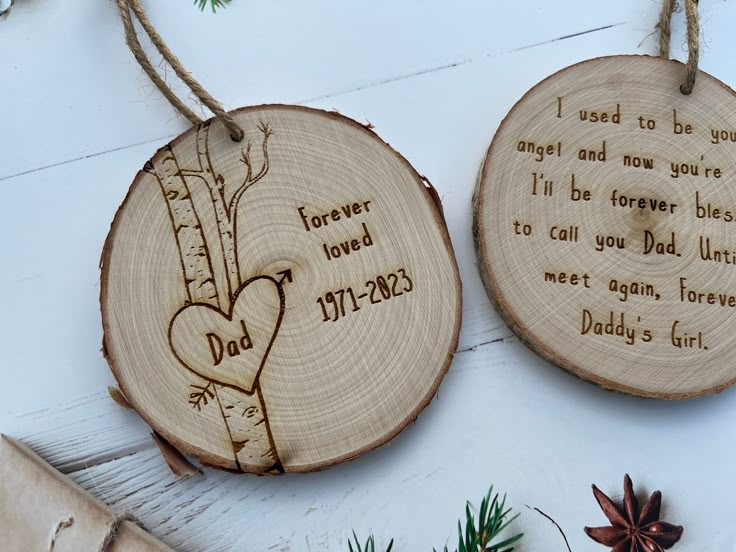 two personalized wood burned ornaments hanging on a white background with pine cones and an evergreen branch