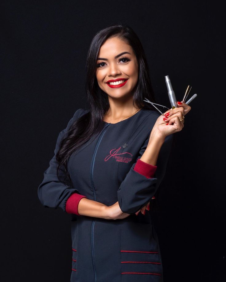 a woman is holding some scissors in her right hand and smiling at the camera while standing against a black background