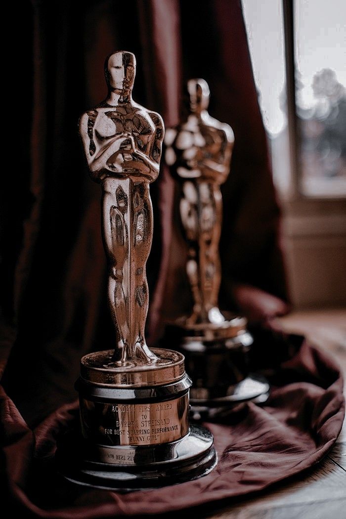 two oscar statues sitting on top of a wooden table next to a red drapes