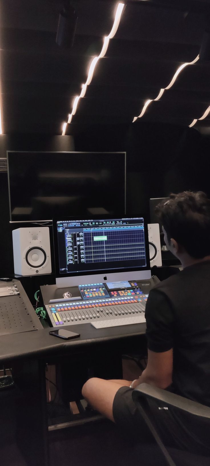 a man sitting at a desk in front of a computer monitor and sound mixing equipment