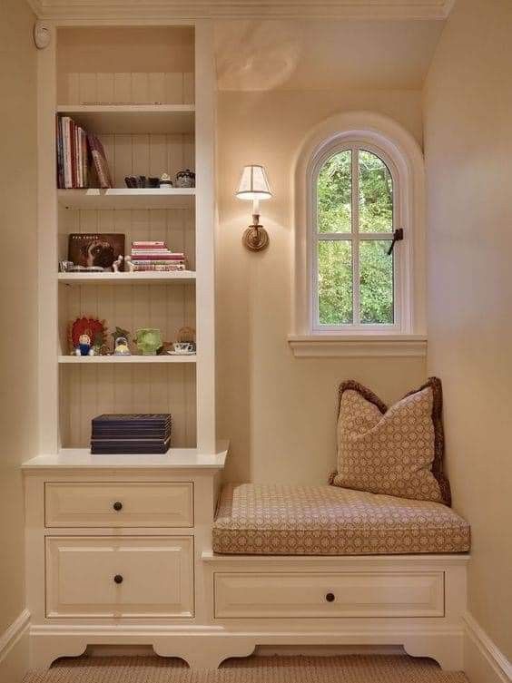 a room with a bench, bookshelf and window