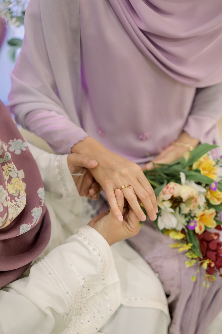 two women in hijabs hold hands over a bouquet of flowers and greenery