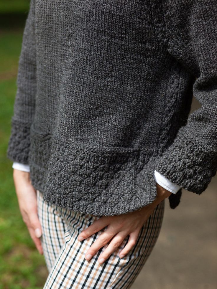 a person with their hands on their hips wearing plaid pants and a gray sweater is standing in the grass