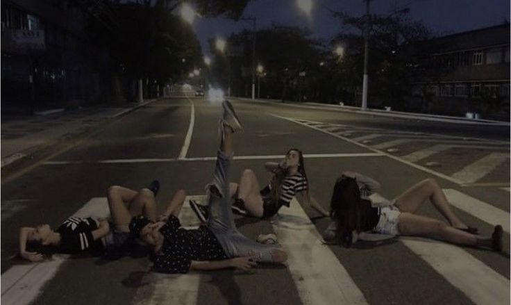 three people laying on the ground in the middle of an empty street at night time