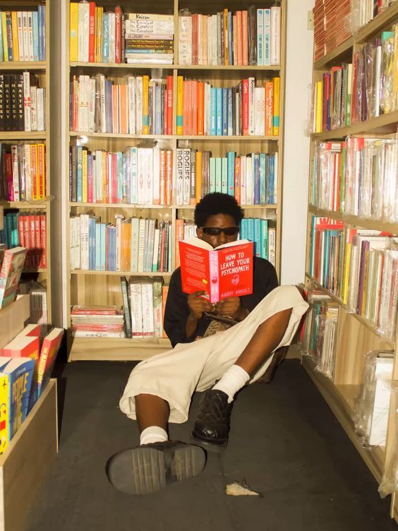 a man sitting on the floor reading a book in front of a bookshelf