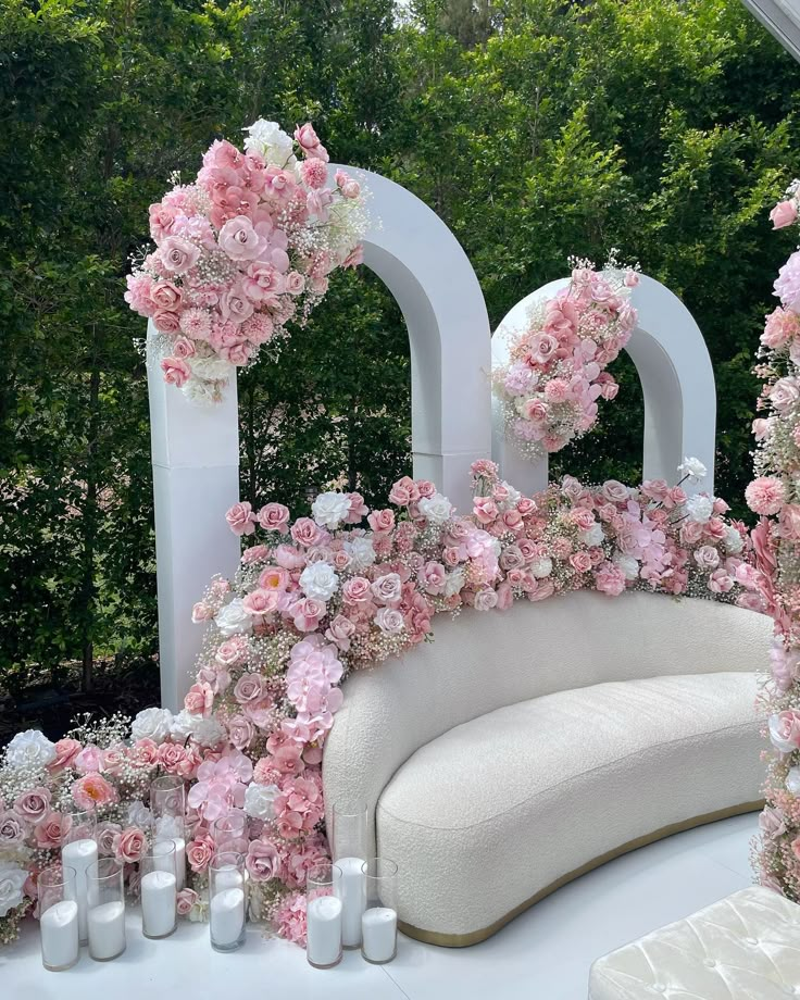 a white couch covered in pink flowers next to candles and greenery on the ground