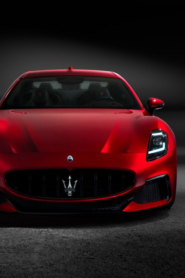 the front end of a red maserato in a dark room with its lights on