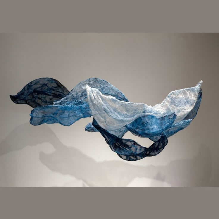 an abstract piece of blue fabric hanging from the ceiling in front of a white wall