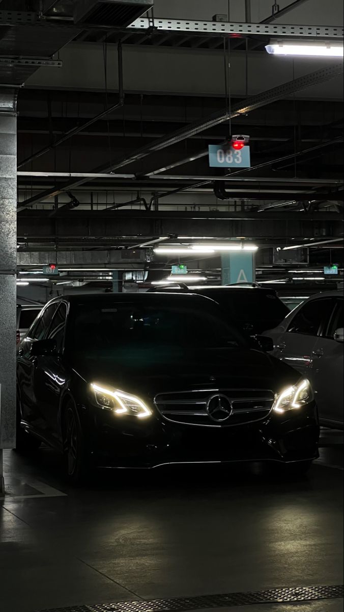 two cars parked in a parking garage with the lights on and one car has its headlight on