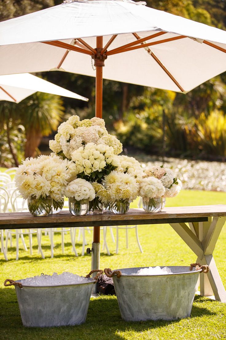 two buckets with flowers are sitting under an umbrella on the grass near chairs and tables