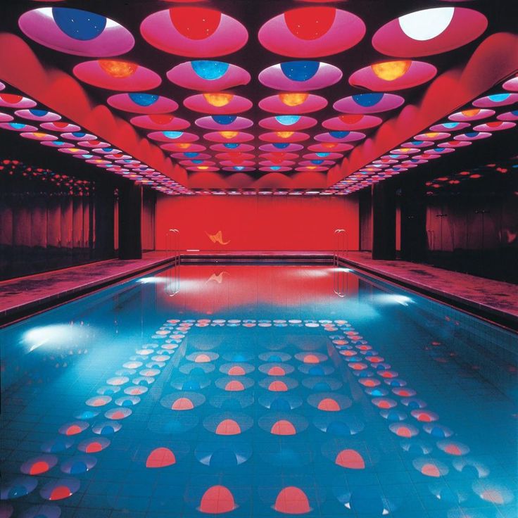 an indoor swimming pool with colorful lights on the ceiling and water reflecting off it's surface