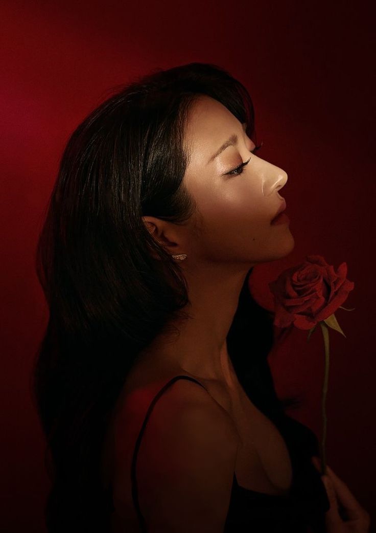 a woman with long black hair and a red rose in her mouth is looking up at the sky