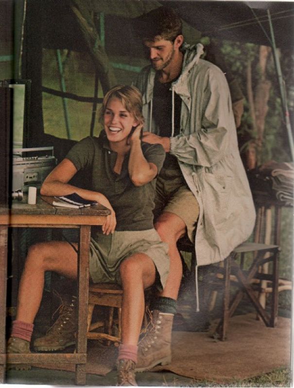 a man standing next to a woman sitting at a table in front of a tent