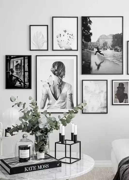 black and white photos hang on the wall above a coffee table with candles, vases and flowers