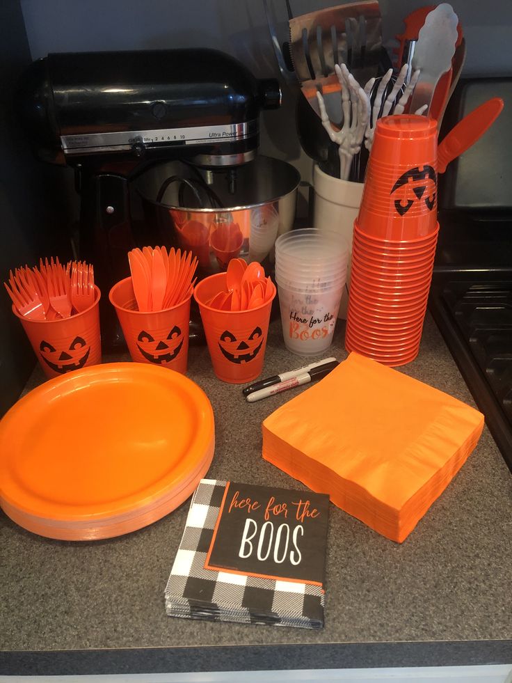 an orange party set up with cups, plates and utensils on the counter