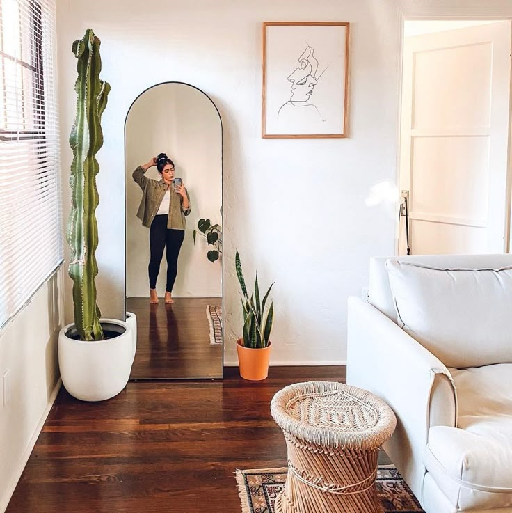 a woman taking a selfie in a mirror next to a couch and cacti