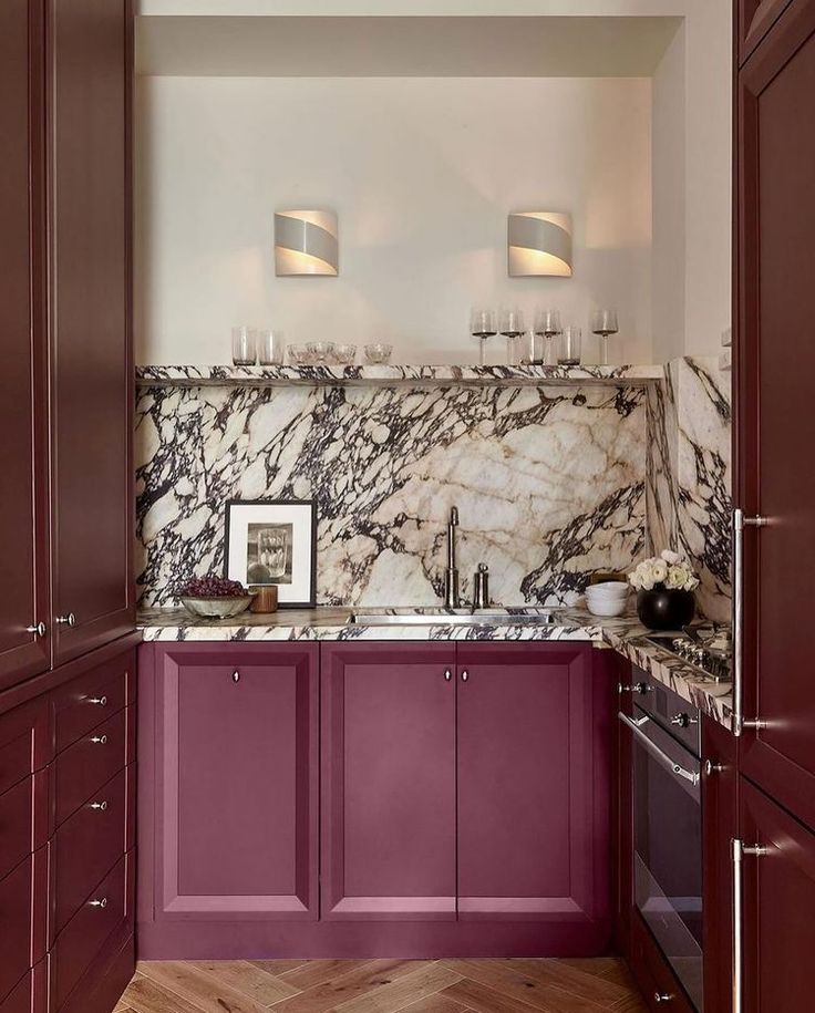 a kitchen with purple cabinets and marble counter tops, along with wine glasses on the sink