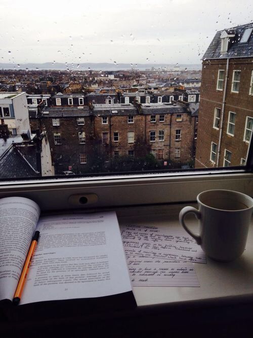 an open book and cup sit on a window sill in front of a cityscape