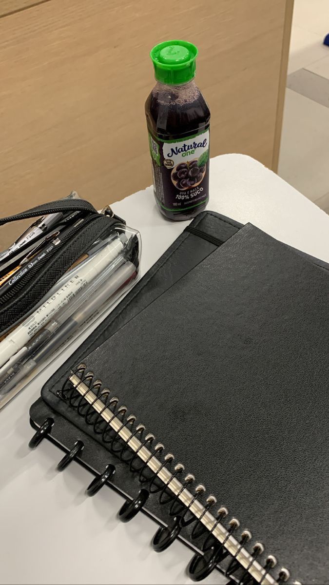 an open notebook and pen on a table next to a black binder with writing utensils