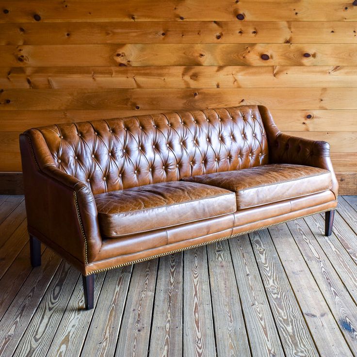 a brown leather couch sitting on top of a wooden floor next to a wood wall