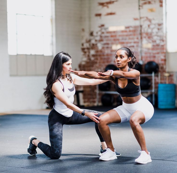 two women in a gym doing squats on the floor with one holding her leg up