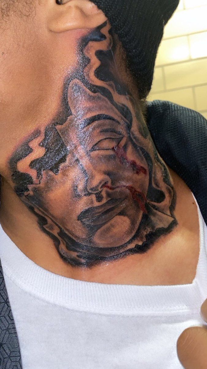 a man with a tattoo on his neck has a face painted black and grey in the background