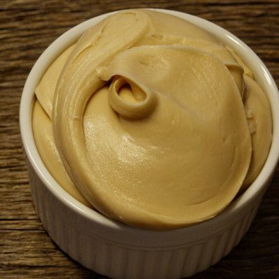 a white bowl filled with yellow cream on top of a wooden table next to a spoon