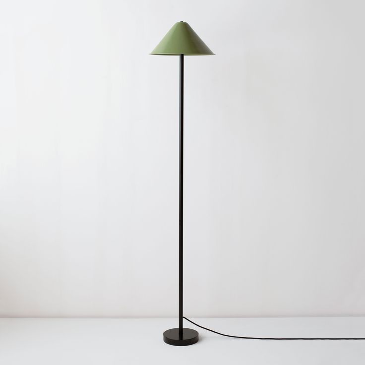 a black floor lamp with a green shade on the base and a white wall behind it