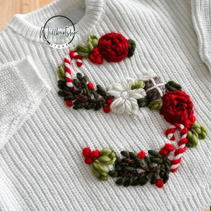 a white sweater with red flowers and green leaves on the collar is sitting on a wooden surface