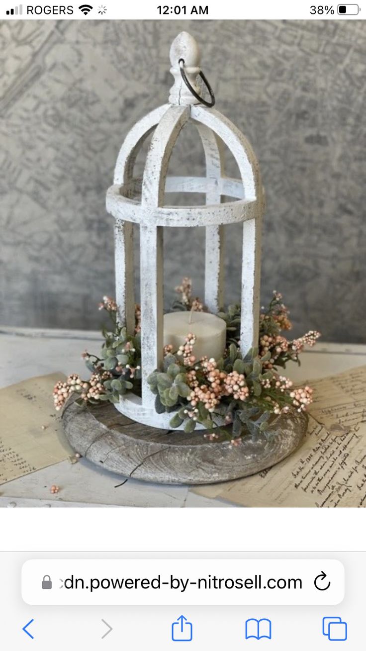 a white birdcage filled with flowers on top of an old book page next to a candle