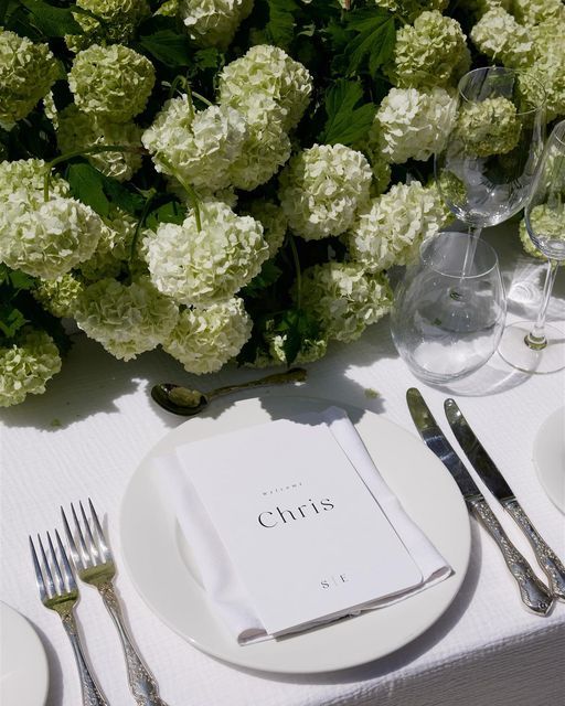 the table is set with white flowers and silverware