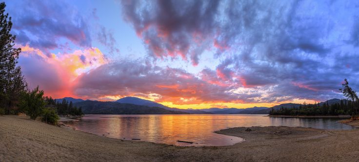 the sun is setting over a lake with mountains in the distance and clouds in the sky