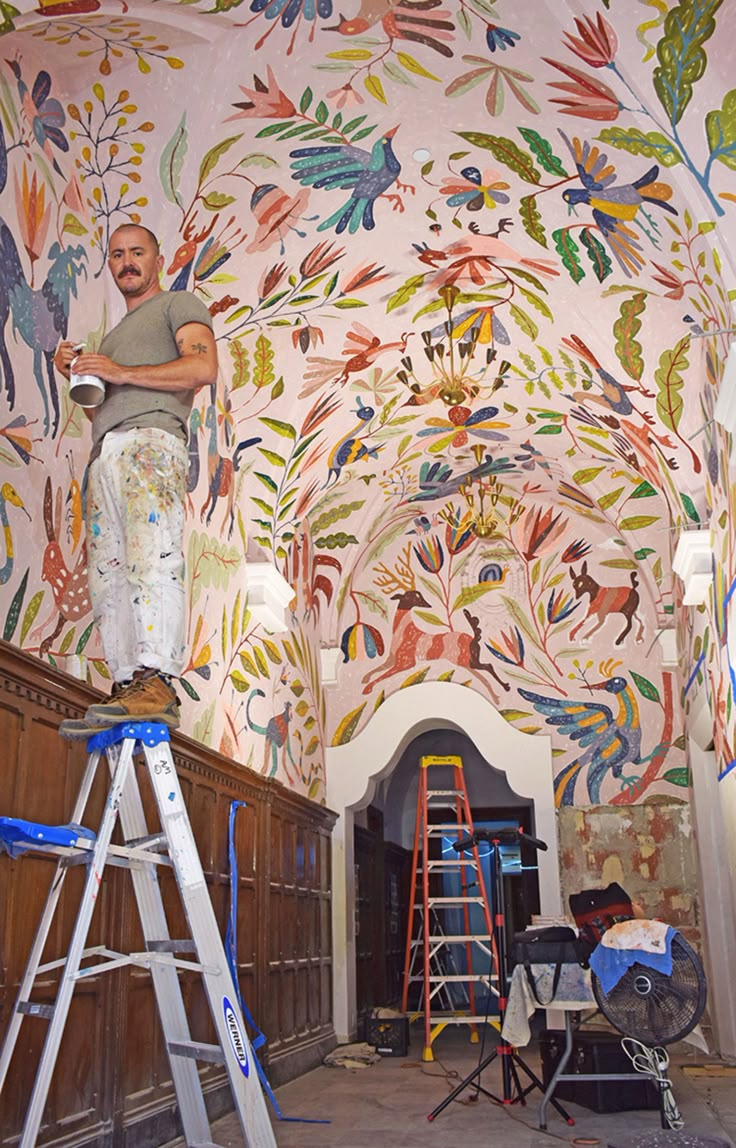 a man standing on top of a ladder in front of a colorful painted wall and ceiling