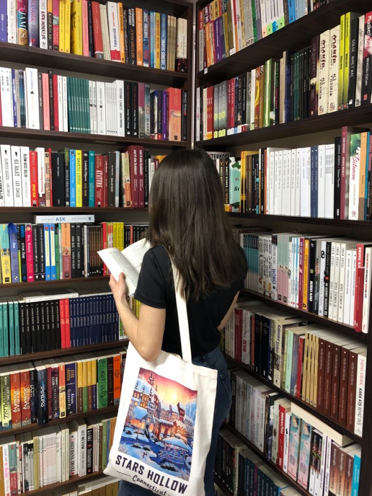 a woman standing in front of a bookshelf with a bag on her shoulder