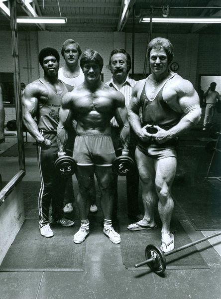 a group of men standing next to each other in front of a mirror with their arms crossed