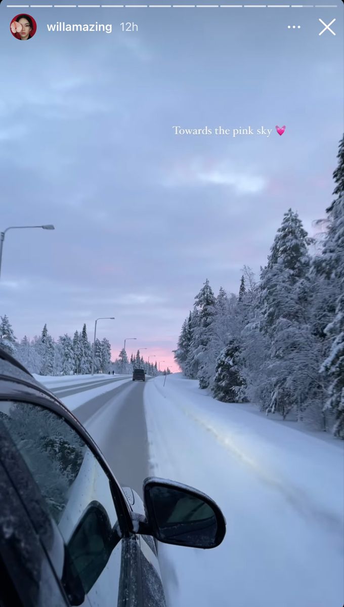 a car driving down a snow covered road next to tall pine trees in the distance